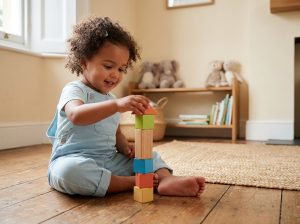 Petite fille de 3 ans concentrée sur un jeu de cubes en bois colorés dans un salon calme et chaleureux