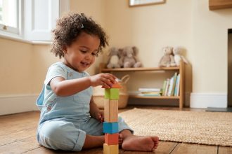 Petite fille de 3 ans concentrée sur un jeu de cubes en bois colorés dans un salon calme et chaleureux