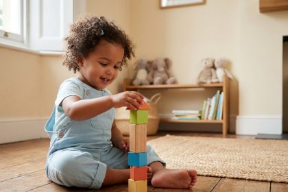 Petite fille de 3 ans concentrée sur un jeu de cubes en bois colorés dans un salon calme et chaleureux